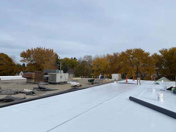 Commercial-Roofing-Contractors-Van-Nuys-CA-California-2 | Shark Roofing Systems Rooftop under construction with a white membrane, HVAC equipment, and a worker, autumn trees in the background.