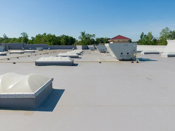 Flat roof with several white HVAC units and skylight domes against a clear blue sky, in a commercial setting.