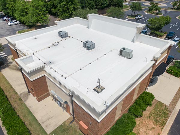 Aerial view of a flat white rooftop on a brick building with three HVAC units and string lights along the edges.