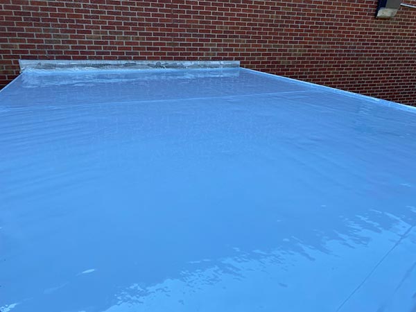 Blue waterproof membrane covering a flat roof, with a red brick wall in the background.